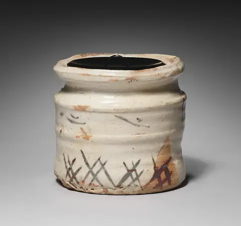 A Mino water jar, cream glaze over a ribbed body brushed with a reed fence in iron brown, capped by a black lacquer lid