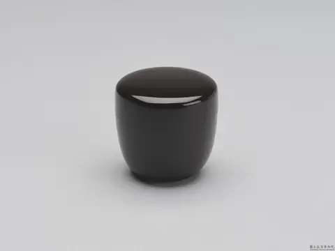 A plain black tea caddy, lid closed against the light