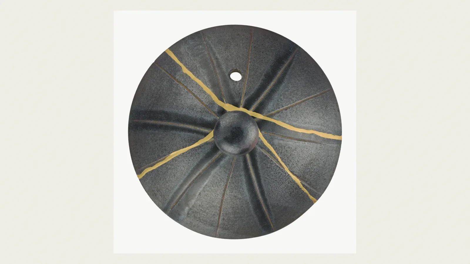 A dark bowl mended with gold, seams radiating across the glaze