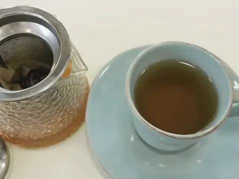 Green tea brewing in a glass pot beside a filled cup