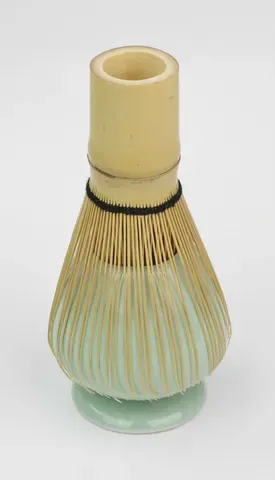 A bamboo whisk standing beside a small tea caddy