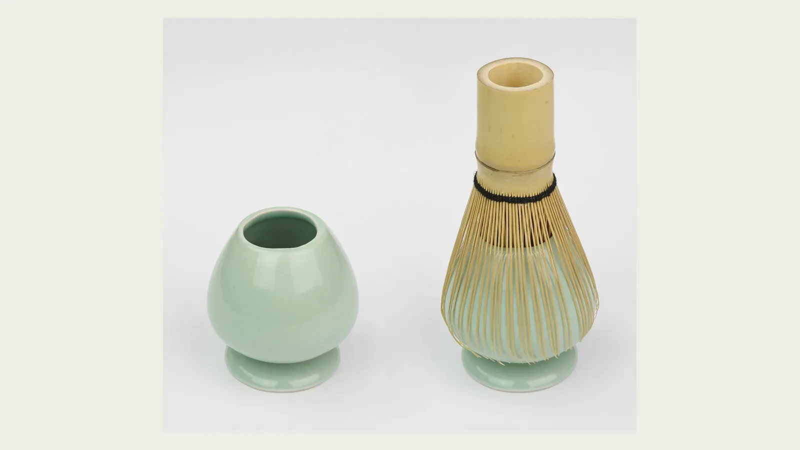 A green tea bowl paired with a bamboo whisk on a white ground