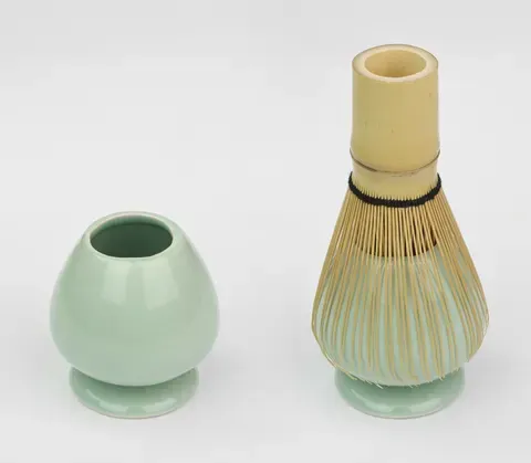 A green tea bowl paired with a bamboo whisk on a white ground