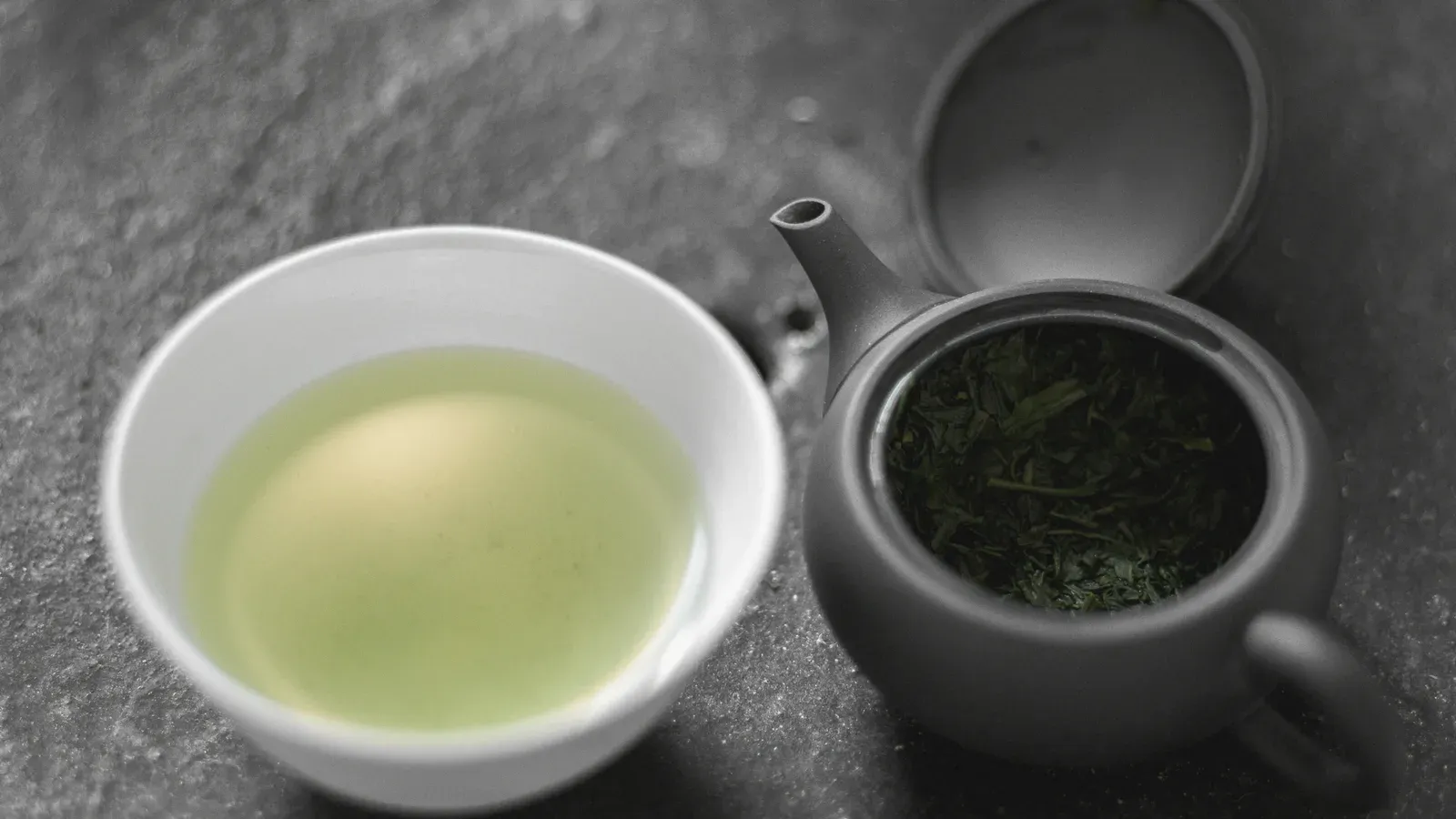 Pale jade gyokuro in a cup beside a dark side-handled pot