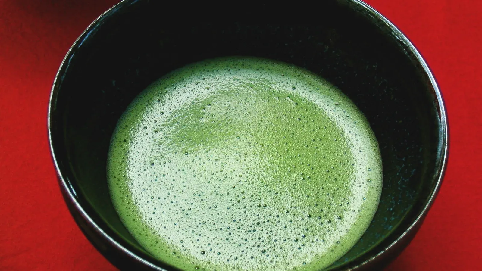 Bright whisked matcha in a black bowl, fine foam across the surface